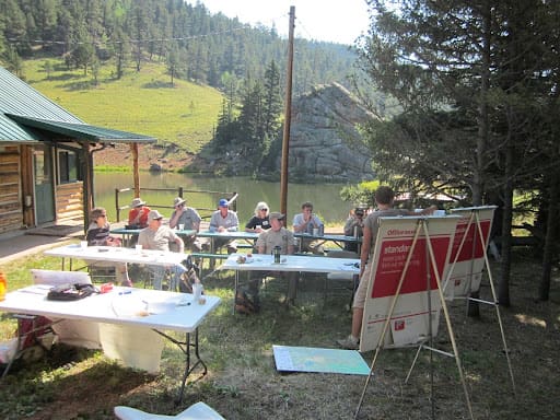 A group of people sitting at tables in the grass.