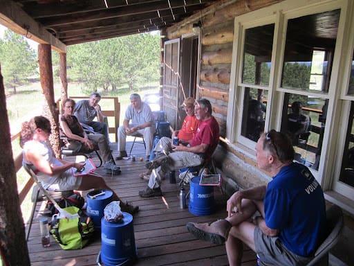A group of people sitting on the porch of a log cabin.