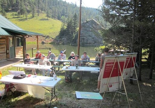 A group of people sitting at tables in the grass.