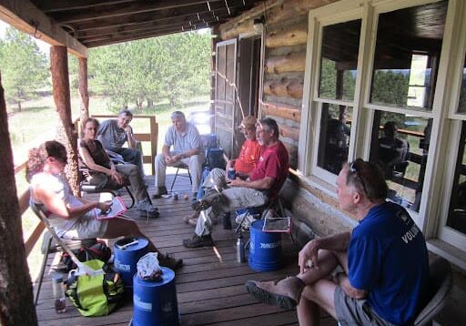 A group of people sitting on the porch of a log cabin.